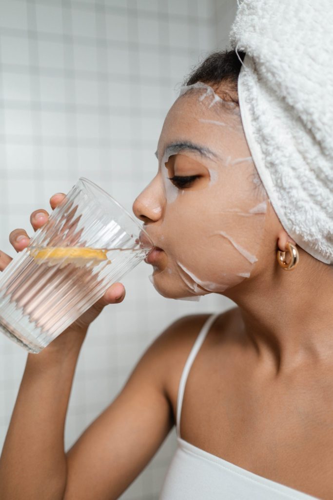 A woman wearing a towel drinking water from a glass.