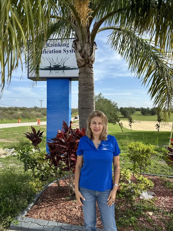 A woman in a blue shirt standing in front of a palm tree, representing our team.