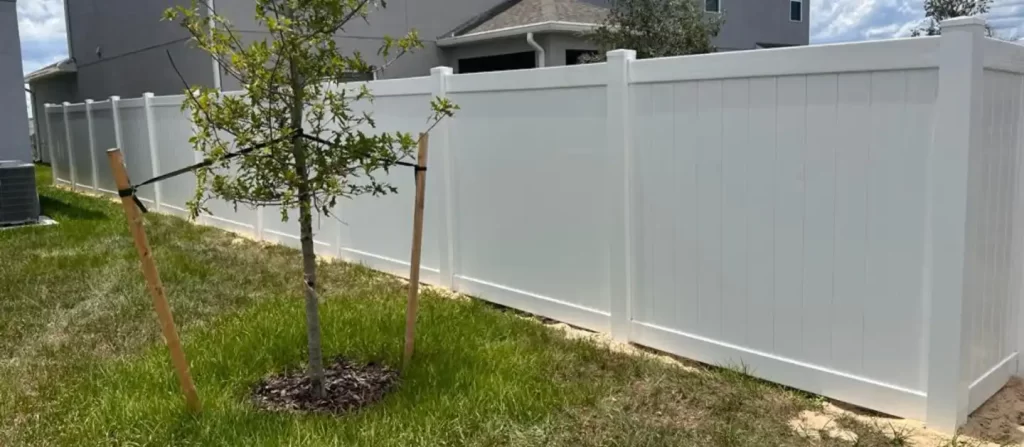 A white fence with a tree in front of it, providing a serene and refreshing ambiance.