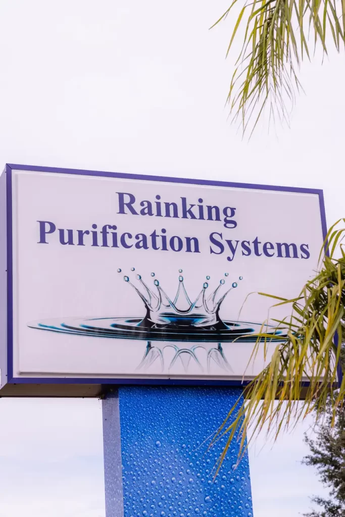 Sign for "Rainking Purification Systems" featuring a splash design, surrounded by palm leaves.