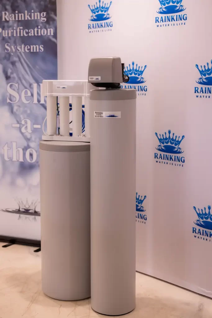 Two cylindrical water purification systems displayed in front of a backdrop with "Rainking Water is Life" logos.