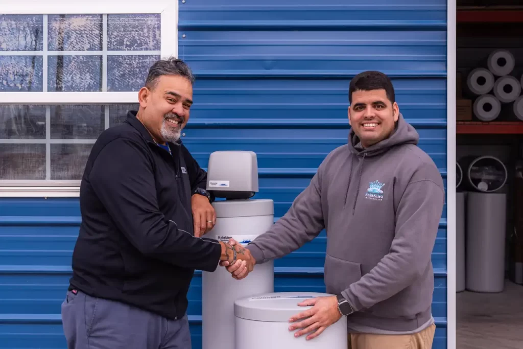 Two men shaking hands in front of a water heater.
